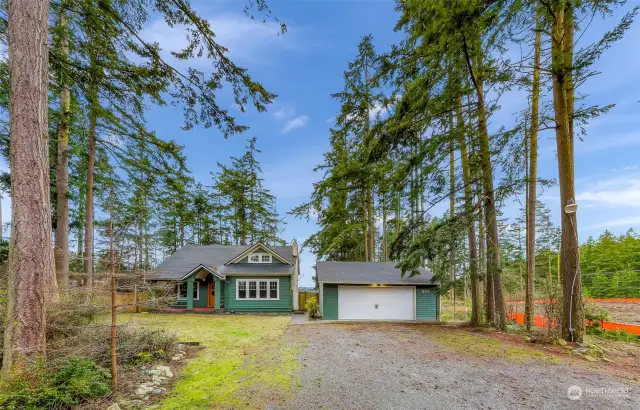 The property’s driveway opens to reveal an expansive yard and a detached garage, offering ample space for outdoor activities and practical living. Surrounded by towering evergreens, this home fosters a sense of seclusion and connection to the outdoors, perfect for embracing a peaceful lifestyle close to nature.