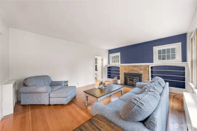 This living room highlights a seamless blend of modern comfort and vintage charm. The built-in shelving around the brick wood-burning stove offers both function and style, while the neutral tones and clean lines make it a flexible space for relaxation or hosting guests.