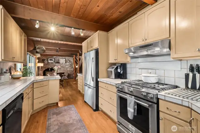 The open-concept kitchen features classic tile counters, newly updated appliances, and a seamless connection to the dining and living areas—perfect for entertaining. New door was installed on the kitchen to the back deck to include a doggie door! The fenced area for pets is off to the left of the kitchen, so super convenient! Beautiful cedar ceilings throughout the main and upper levels.