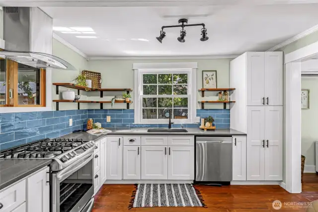 Modern kitchen with quartz counters, ceramic tile back splash, stainless steel appliances, and reclaimed wood open shelving.