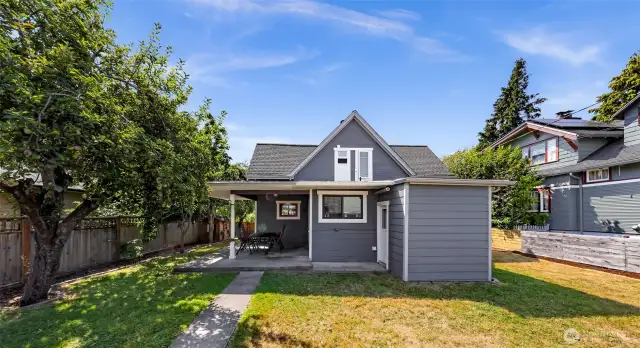 Large fully fenced back yard with covered patio, fire pit, fruit trees, and raspberry bushes.