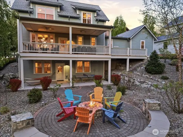Exterior twilight view of home and outdoor living area with custom built-in fire table, lower patio with hammock, and ping pong table and upper lake view decks with BBQ, dining and lounge area with fire table.