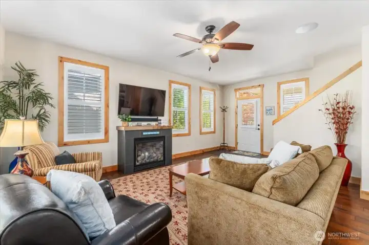View 1 of living room with engineered wood flooring, oversized windows and fireplace.