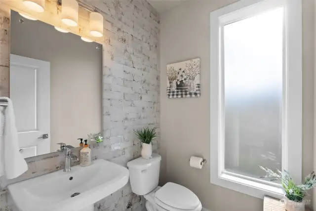 The main level powder room is a stunning showcase of thoughtful design, highlighted by the filtered light that gently streams through frosted glass, creating a soft and inviting ambiance.  The floor to ceiling tiled wall is a beautiful focal point to this well used space.