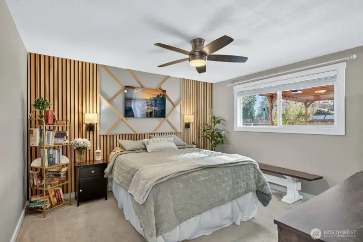 Primary Suite with designer slated wall, ceiling fan, and window with blinds.