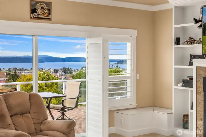 Luxury plantation shutters frame a west-facing panoramic view of Hood Canal, while sliding glass doors open to the expansive deck for seamless indoor-outdoor living.