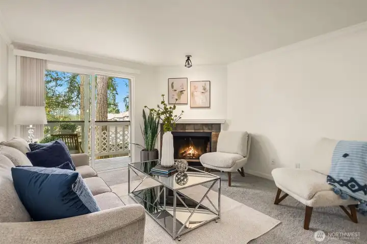 A bright, inviting living room with a wood-burning fireplace and beautiful natural light from the lush green area just outside