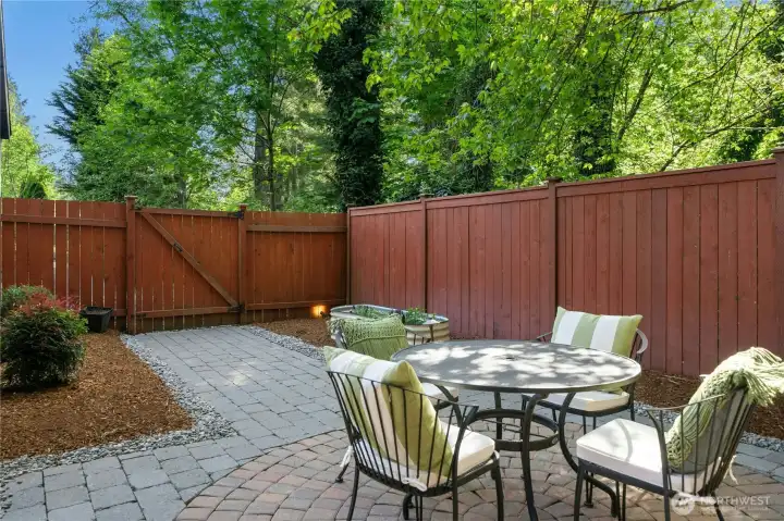 Fully fenced rear yard with extensive paver patio, garden bed, and mature landscaping.