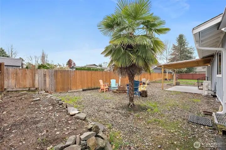 North end of backyard features a large rocked lined raised garden bed, established palm tree and firepit area.