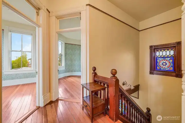 Assending stairwell primary retreat showcasing transom windows, hardwood floors and archway to additional room.