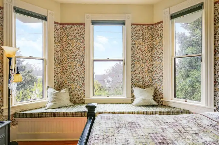 Upstairs bedroom with a built-in-window seat framed by three windows, bringing in light.  The original floor continue through this room and original wood trim set this home's era.