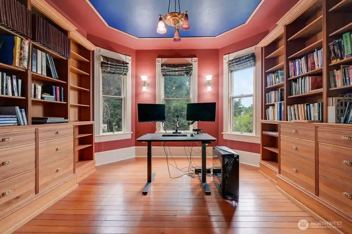 A light filled library room with large windows, built-in shelving and a distinctive ceiling detail, well suited for workspace or study.