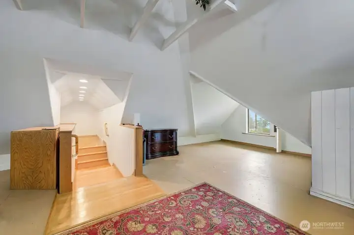 Top-floor room with sloped ceilings, exposed beams, and natural light defining this area.