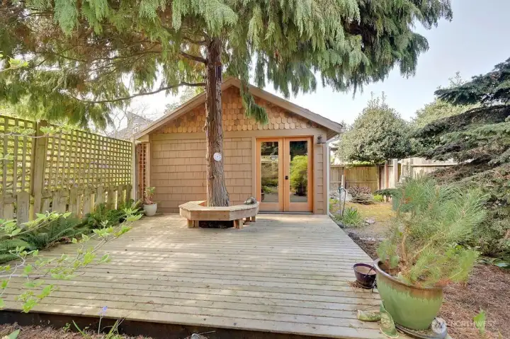 Refurbished outbuilding using sustainable materials, with wood decking, custom bench and glass paneled doors.