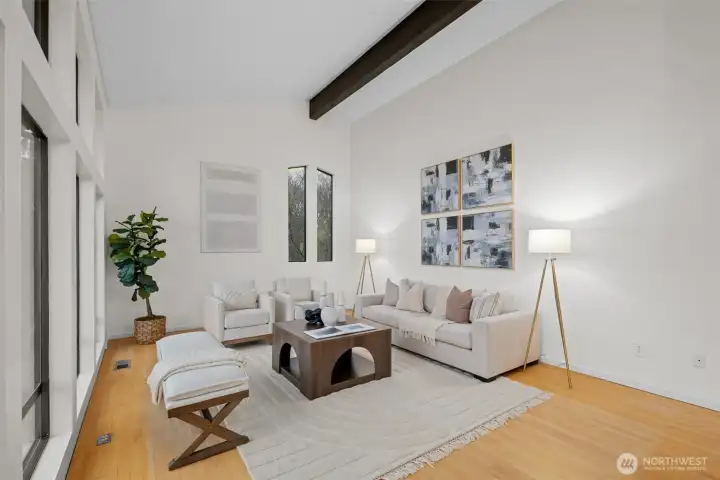 Enjoy entertaining here, or relax with family or spoil your guests in comfort and style. Light colored walls lift the spirit and brighten the space. Two story view windows fill the room with beautiful natural light and look out toward the mountains and the Puget Sound. The soaring ceiling and warm wood floors create an airy, uplifting atmosphere that feels both peaceful and refined. A pair of tall accent windows adds soft, filtered light on the opposite wall, and exposed beams lend the room a timeless architectural charm.