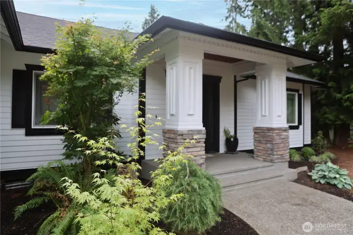 A Japanese maple and lush greenery frame the covered entry, where stone-wrapped columns add warmth and texture to the home's exterior. A Japanese maple and lush greenery frame the covered entry, where stone-wrapped columns add warmth and texture to the home's exterior.