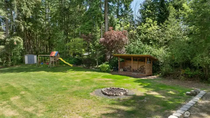 The backyard invites every kind of gathering, from evenings around the fire pit to playtime on the lawn, with wood storage, useful outbuildings, and a treed backdrop that gives the space a private Northwest feel.
