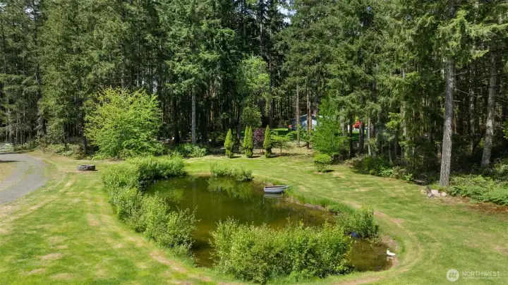 The front yard feels like its own private retreat, with a pond, small boat, mowed lawn, mature landscaping, trees, and ferns creating a setting that feels peaceful and full of possibility.