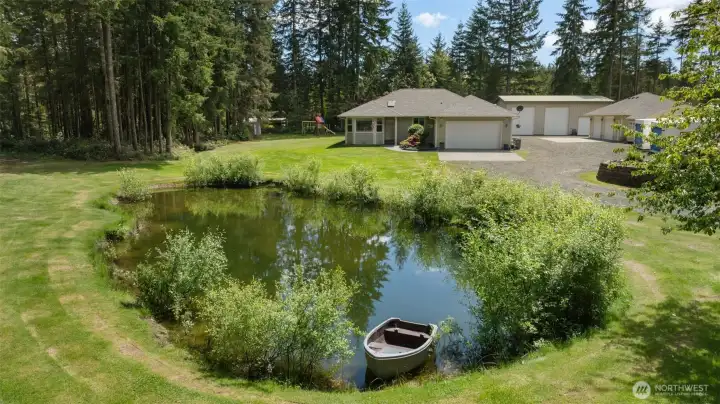 A storybook view of the home, pond, shops, and backyard play space, with simple joys like frog songs, salamanders, and wildlife around the water adding to the property’s everyday charm.