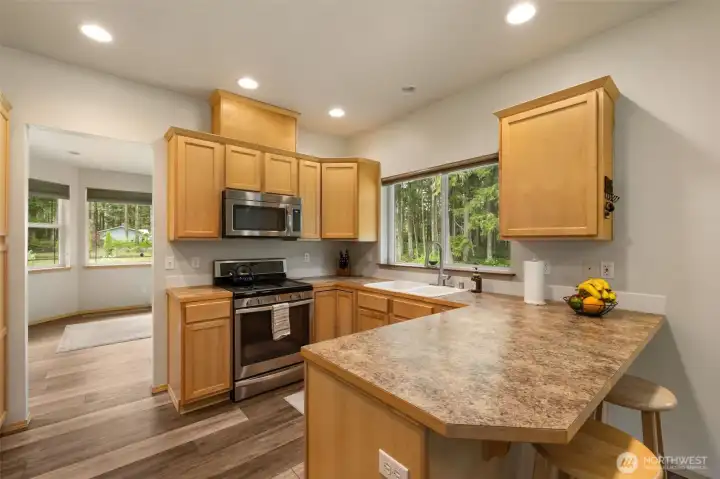 A smart, connected kitchen layout keeps everything within easy reach, from the gas range and double sink to the breakfast bar, all framed by a large window looking out to the trees.