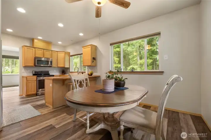 The dining area feels bright, simple, and inviting, with continuous wood grain laminate floors, clean lines, and peaceful tree views that make daily meals feel connected to the setting.