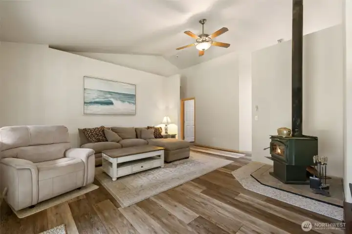 A bright family room with vaulted ceilings, warm wood grain laminate floors, and a wood stove creates an easy gathering place for cozy evenings, casual weekends, and everyday connection.