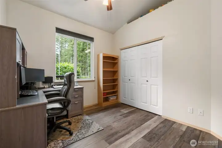 A flexible third bedroom works well as an office, guest room, or creative space, with vaulted ceilings, wood grain laminate floors, a generous closet, and peaceful tree views that make the room feel open and calm.