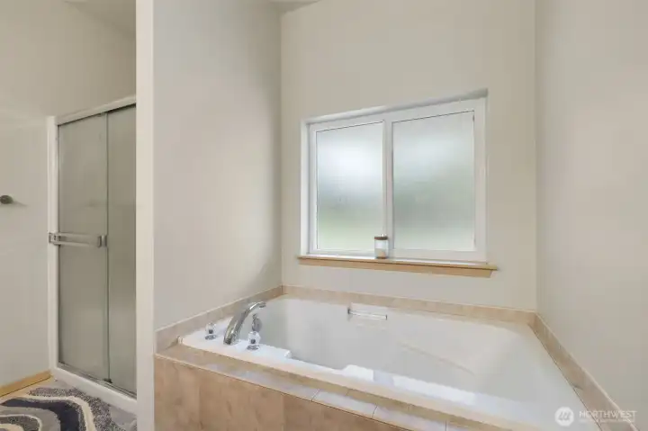 A tile wrapped soaking tub and separate glass shower give the primary bath a spa inspired feel, with natural light filtering through the frosted window for comfort and privacy.