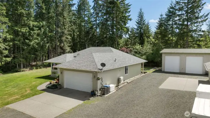 This aerial view highlights the flexibility of the property, with ample parking, garage space, a large shop, and a peaceful backdrop of trees and sky that makes the setting feel both useful and secluded.