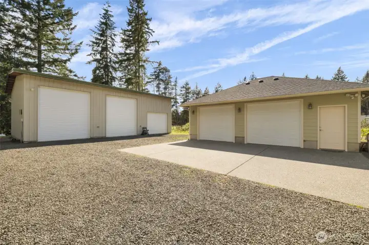 From the ground level, the shop setup feels even more impressive, with multiple garage bays, easy access doors, lighting, concrete parking, and fresh gravel creating a highly functional space for work, storage, vehicles, and projects.