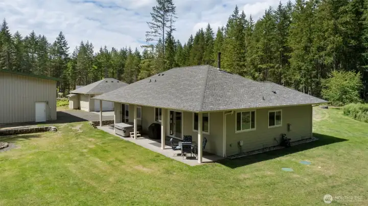 The covered back patio extends the living space outdoors, creating an easy place to relax, gather, enjoy the hot tub, and take in the lawn, shops, and peaceful property setting.