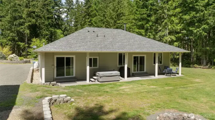 A closer look at the covered back patio shows how the home opens to outdoor living, with the hot tub and two sliders connecting the family room and primary bedroom to the backyard.