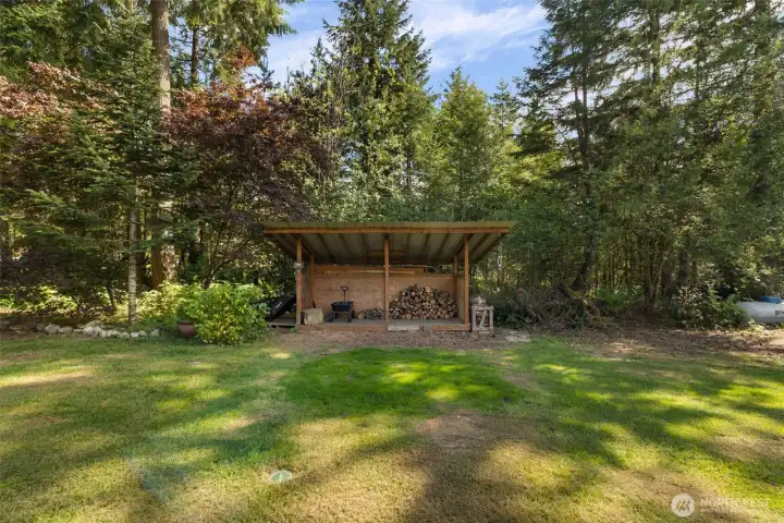 A dedicated wood shed keeps firewood dry, organized, and ready for the wood stove and fire pit areas, adding practical charm to the tree lined backyard.