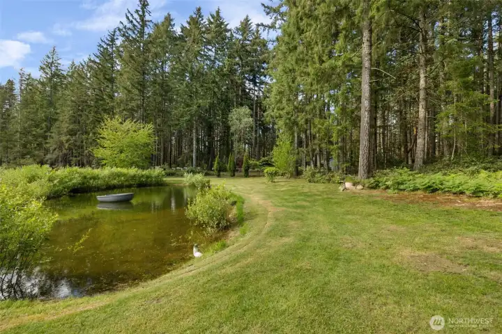 A scene that feels pulled from a Northwest lifestyle magazine, where the pond, rowboat, ferns, trees, and open sky create the kind of peaceful setting buyers hope to find but rarely do.