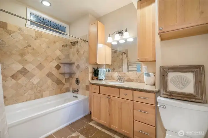 Large main floor bathroom with tile, a 6 ft long tub and a heated towel bar great storage and a stained-glass window.