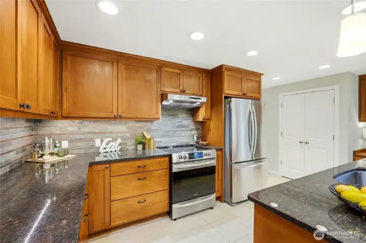 The kitchen also features stainless steel appliances, abundant storage, and a beautiful tile backsplash. The double doors in the background open to the pantry.