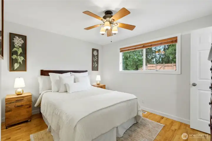 Relax in the freshly painted primary suite featuring hardwood floors, a ceiling fan, and tranquil views of the private backyard.