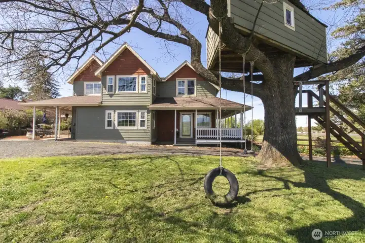 Charming exterior view of the home showcasing wraparound porch and a tree house!