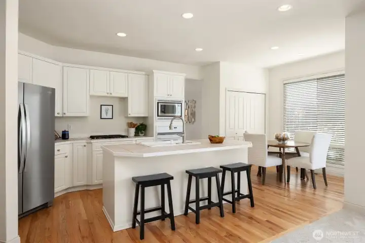 Bright, airy kitchen showcasing crisp white cabinetry, a spacious island with seating, recessed lighting, and great appliances.