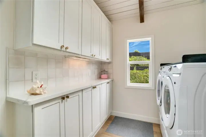The laundry room features floor-to-ceiling white cabinetry, quartz counters, tile backsplash, and a shiplap ceiling with exposed beam The laundry room features floor-to-ceiling white cabinetry, quartz counters, tile backsplash, and a shiplap ceiling with exposed beam