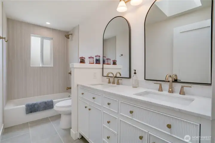 The hall bath is no afterthought — double vanity with fluted cabinetry, quartz counters, dual arched mirrors, designer tile, and gold hardware. No compromise on finish quality anywhere in this home. The hall bath is no afterthought — double vanity with fluted cabinetry, quartz counters, dual arched mirrors, designer tile, and gold hardware. No compromise on finish quality anywhere in this home.