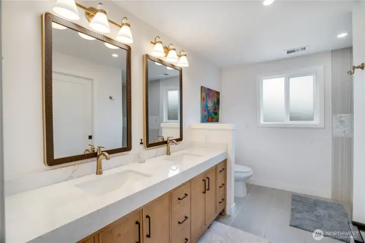 Double vanity with fluted cabinetry, quartz counters, arched black-framed mirrors, skylight, and brushed gold fixtures throughout. Double vanity with fluted cabinetry, quartz counters, arched black-framed mirrors, skylight, and brushed gold fixtures throughout.