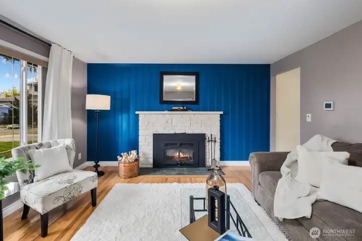 Living room with large windows, fireplace, and accent wall. Natural light and open layout create a comfortable main gathering space.