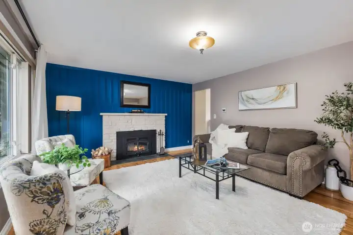 Living room with large windows, fireplace, and accent wall. Natural light and open layout create a comfortable main gathering space.