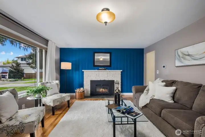 Living room with large windows, fireplace, and accent wall. Natural light and open layout create a comfortable main gathering space.