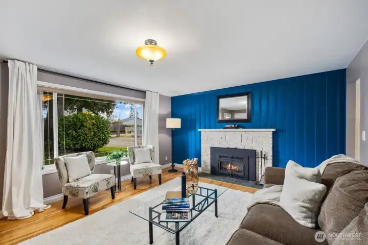 Living room with large windows, fireplace, and accent wall. Natural light and open layout create a comfortable main gathering space.
