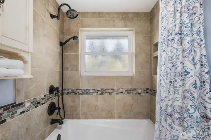 Bathroom with updated vanity, mirror, and tiled tub surround. Clean layout with practical fixtures and storage.