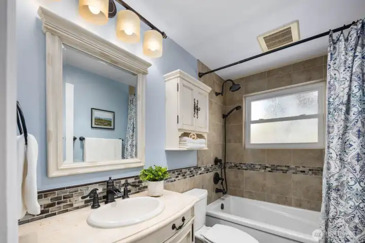Bathroom with updated vanity, mirror, and tiled tub surround. Clean layout with practical fixtures and storage.