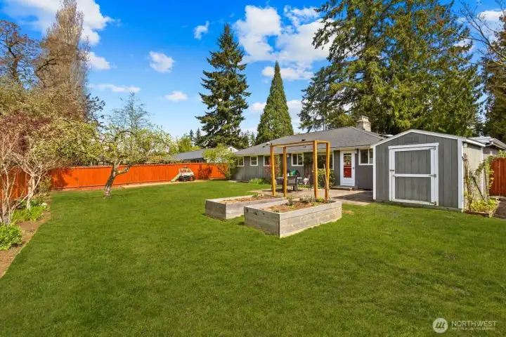 Large backyard with lawn, raised garden beds, and detached structure for storage or additional use. Outdoor space supports a variety of activities.