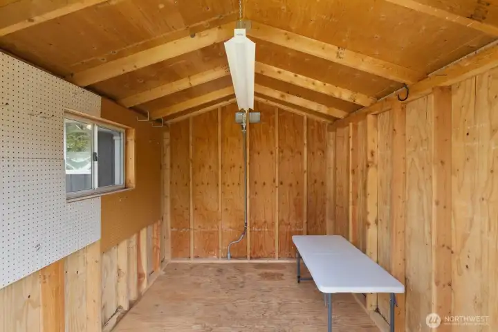 Detached storage shed with wood interior, overhead lighting, window, and built in pegboard for organization. The versatile space provides practical room for tools, equipment, hobbies, or additional storage.
